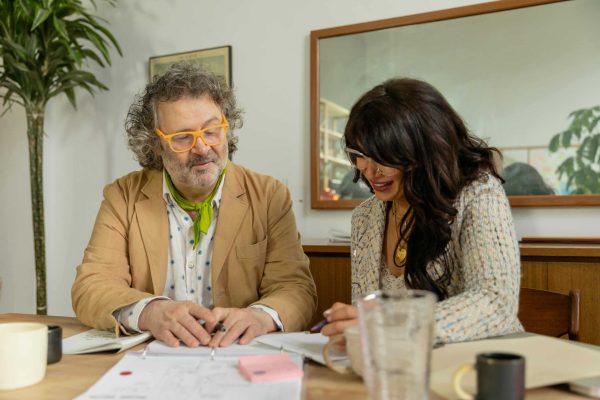 Two colleagues discuss ideas in an office with documents and coffee on the table.